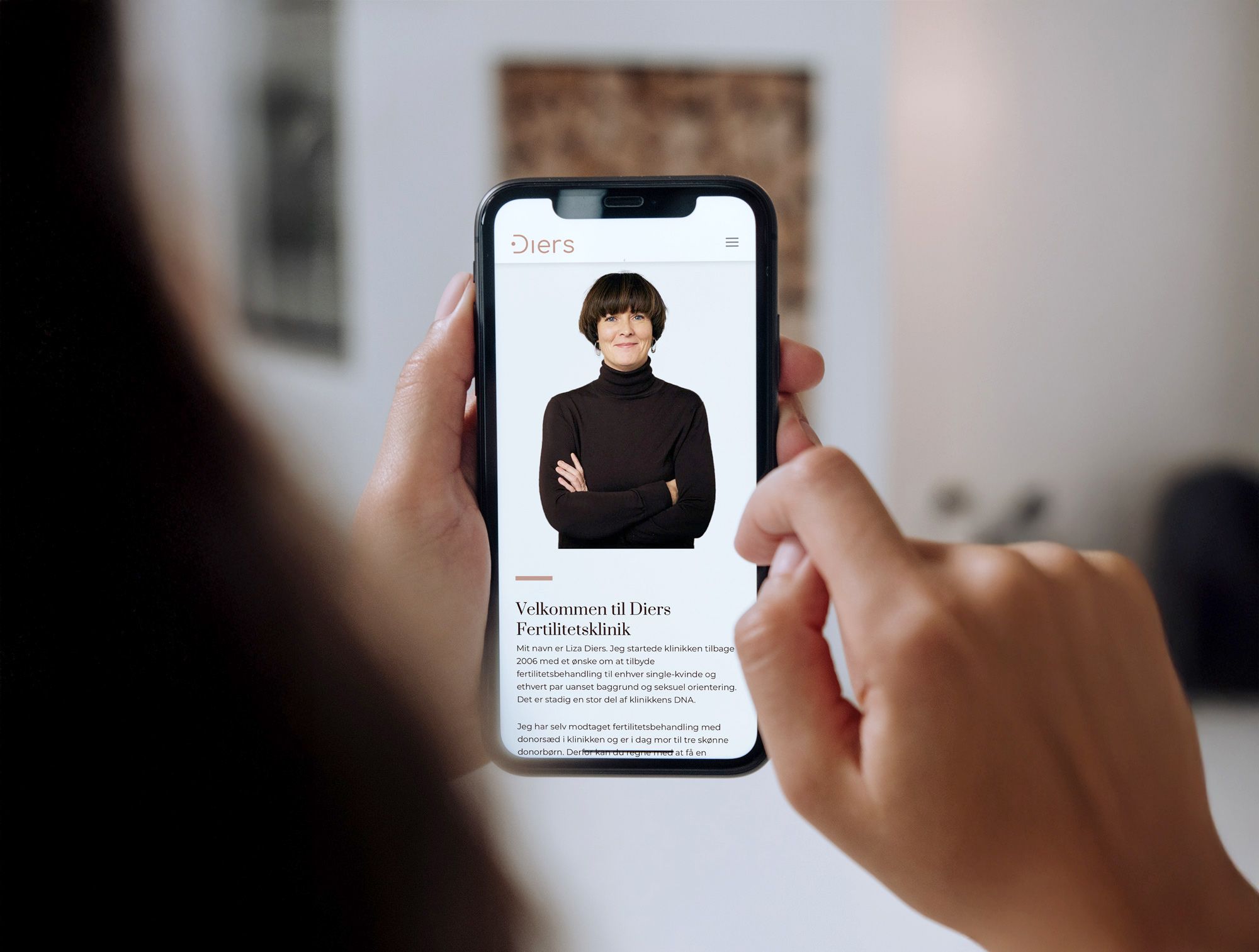 Billedet viser en kvinde som sidder med sin telefon i hånden, som viser Diers Fertilitetskliniks hjemmeside