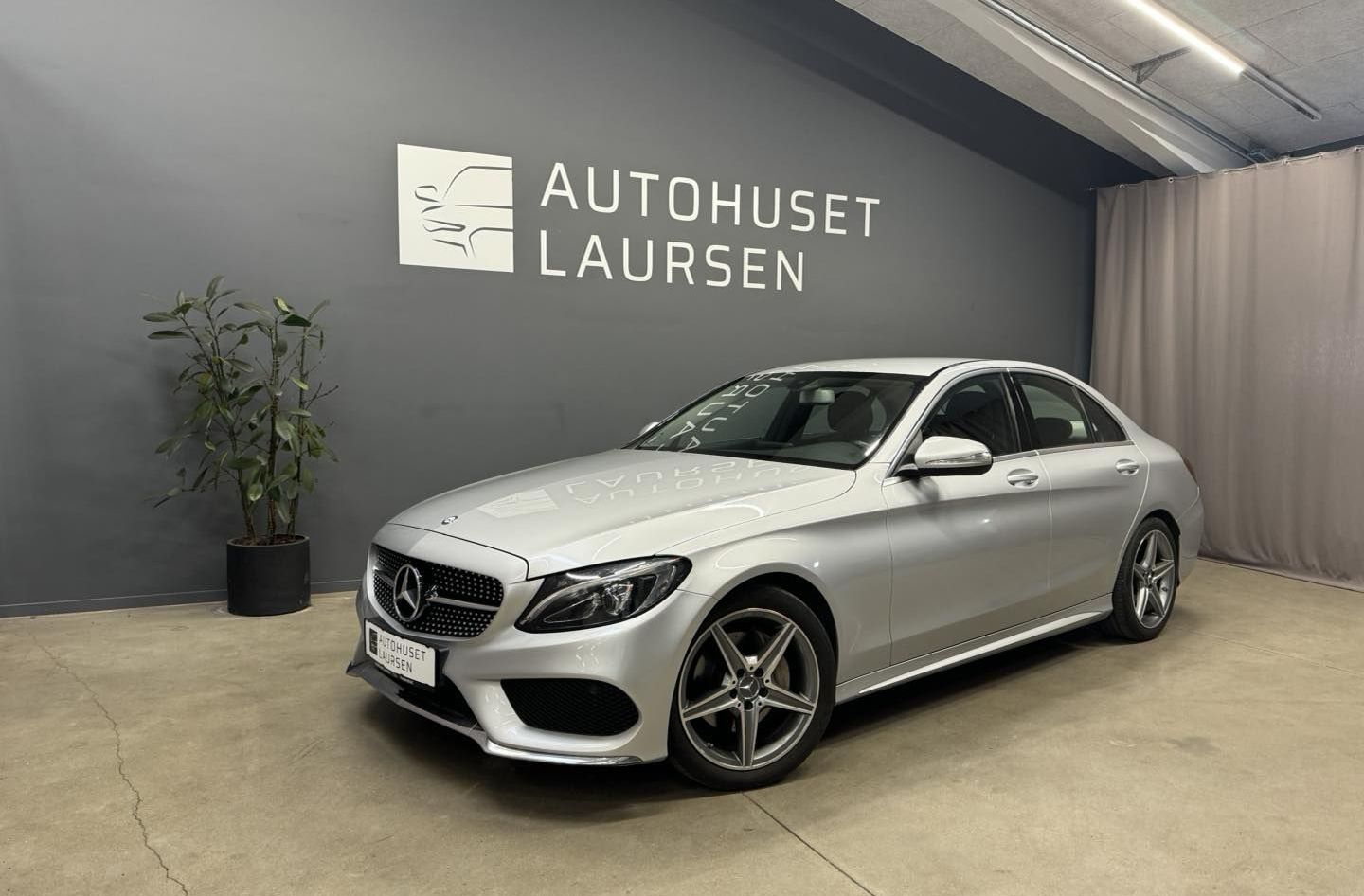 Sølvfarvet Mercedes-Benz parkeret i en udstillingshal med skiltet 'Autohuset Laursen' på væggen