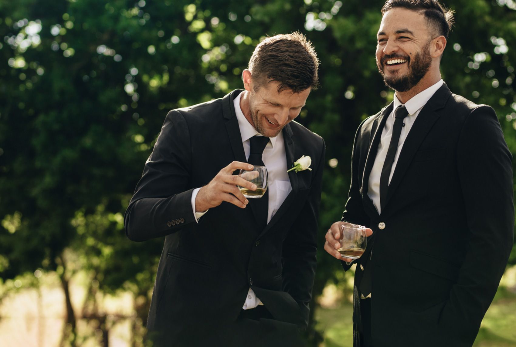 To mænd i jakkesæt griner og nyder en drink til en udendørs festlig begivenhed