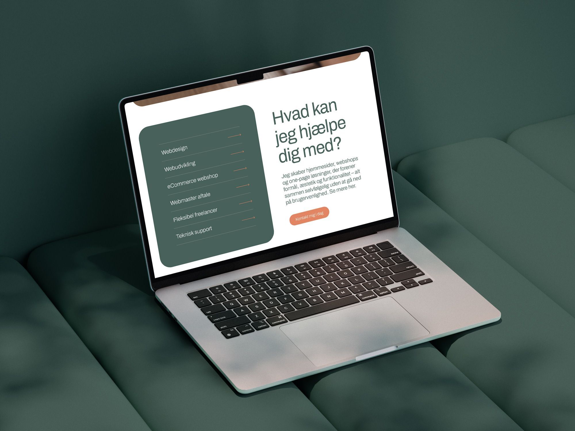 Åben laptop på en grøn sofa viser en hjemmeside med en hjælpesektion og en rød call-to-action-knap